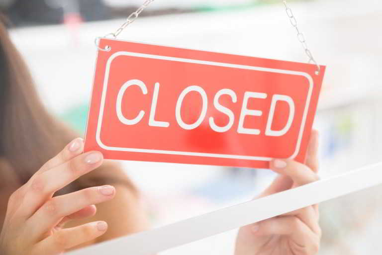 Closeup of female owner holding closed sign in clothing store